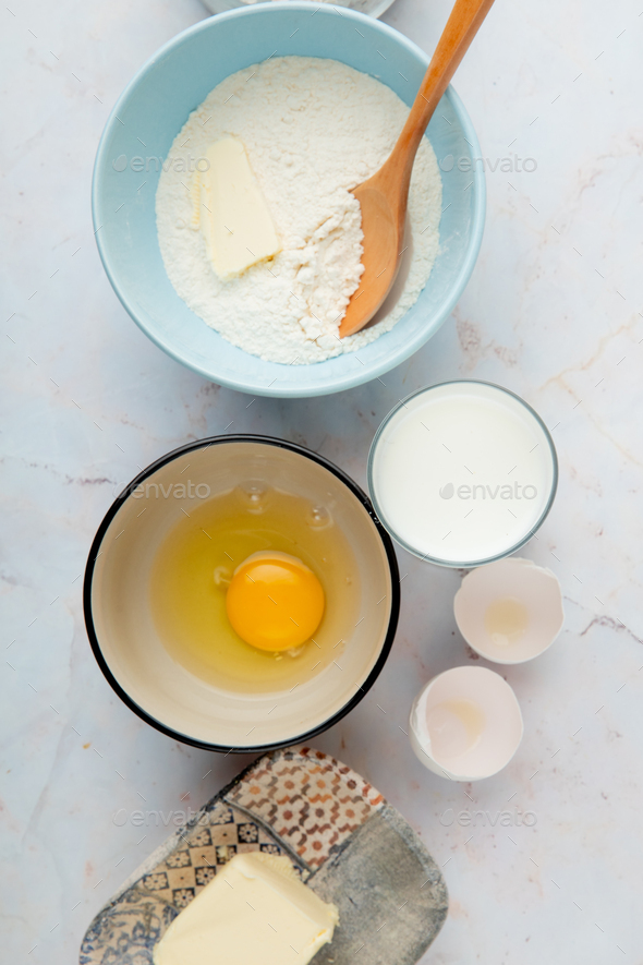 top view of bowl with egg yolk and butter with flour, milk, eggshell on